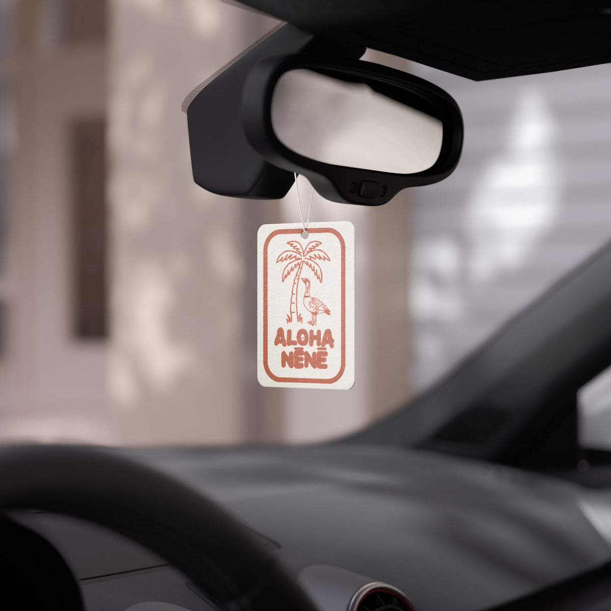 Car air freshener hanging from a car's rearview mirror with a blurred background.