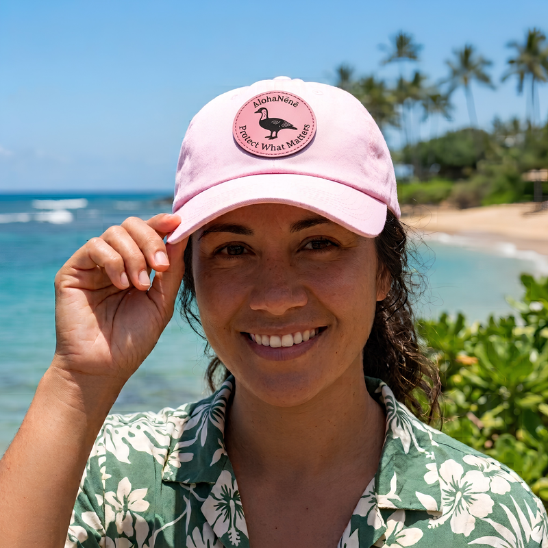 Aloha Nēnē trucker hat resting on tropical monstera leaves in a lush Hawaiian-inspired setting. The hat features a cream crown, black brim, and bold black embroidered Aloha Nēnē logo with a shaka symbol. Natural sunlight highlights the premium stitching and relaxed island lifestyle aesthetic, with vibrant green foliage softly blurred in the background.